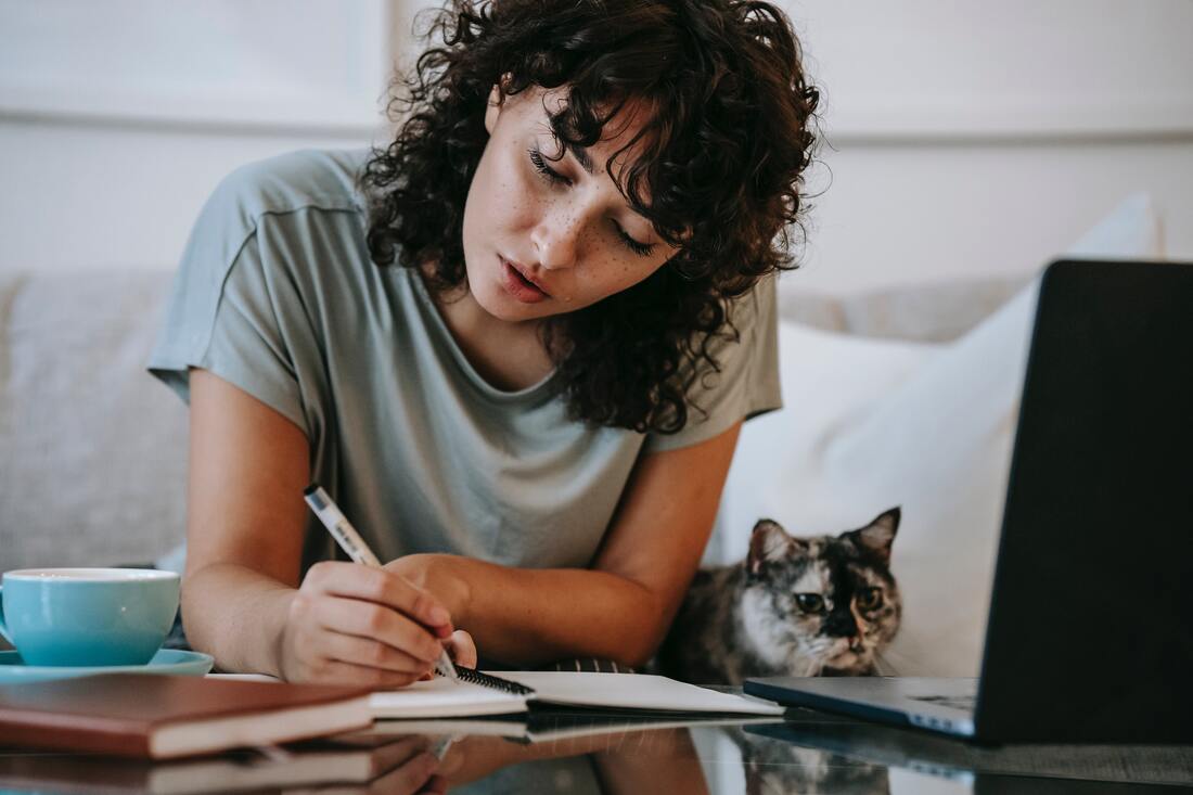 Woman writing in notebook with cat next to her