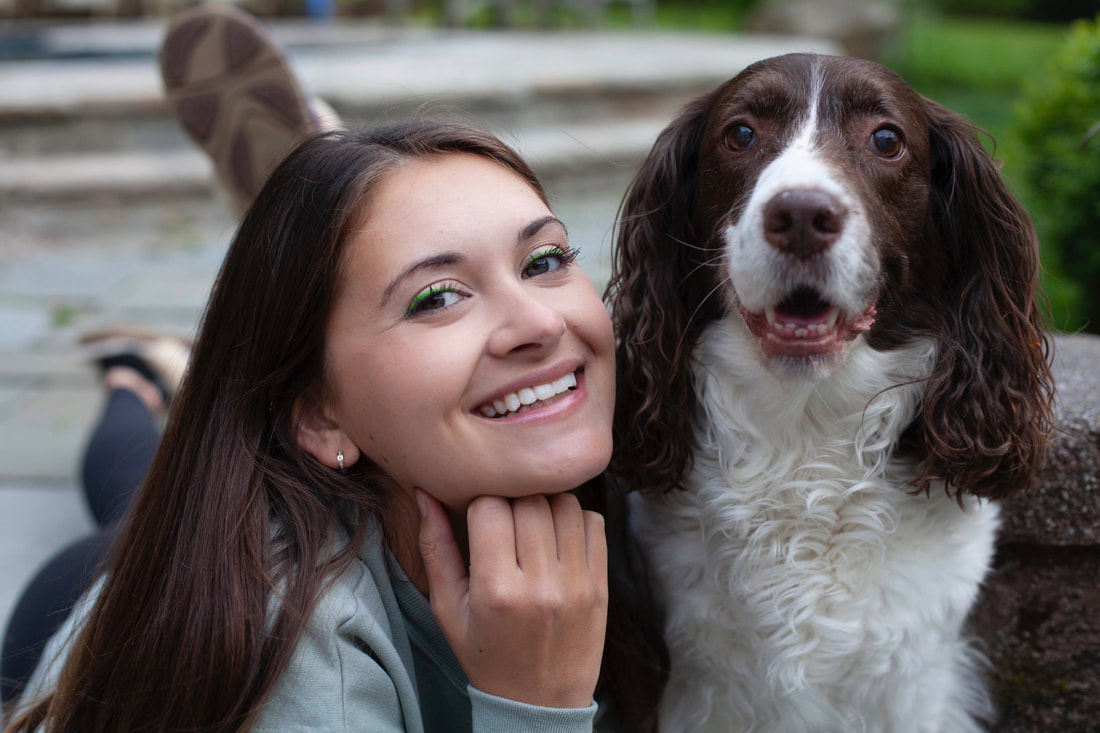 Brunette woman in twenties smiling next to brown and white hound, both looking at camera